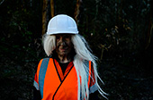 Jill Orr in costume, ina a high vis vest and hard hat with a dirty face, standing in a river bed.