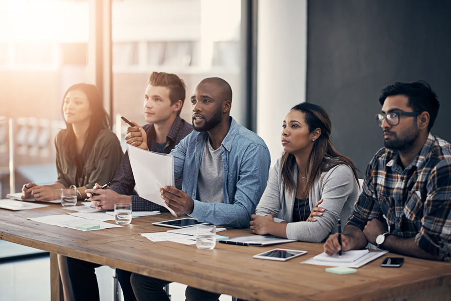 Five people sitting at a long desk looking at a presentation off screen.