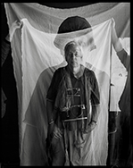 Photo of Tim Page standing in front of portrait dressed as a war photographer 